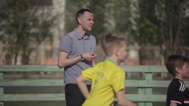Bobruisk, Bielorrusia - 15 de junio de 2019: Joven entrenador de fútbol masculino o de fútbol viendo a su equipo de niños jugar en un hermoso campo de fútbol . — Vídeos de Stock