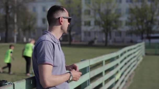 Bobruisk, Bielorrusia - 15 de junio de 2019: Joven entrenador de fútbol masculino o de fútbol viendo a su equipo de niños jugar en un hermoso campo de fútbol . — Vídeos de Stock