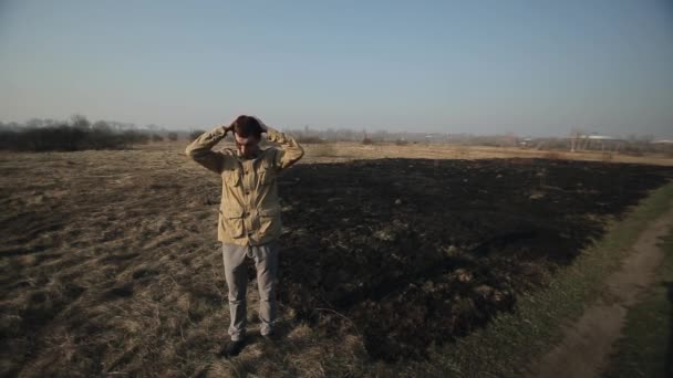 Muž stojí na pozadí spálené trávy a skřípne hlavou. Slzy na hlavě a lítost, že se rozhořčením rozhněval kvůli zničení přírody — Stock video