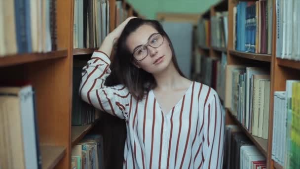 Porträt eines jungen schönen Mädchens in der Bibliothek. Studentin studiert zwischen vielen Büchern zwischen Regalen. — Stockvideo