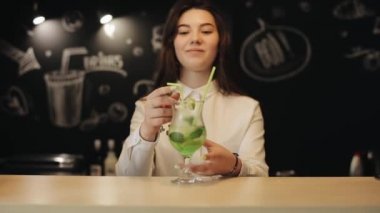 Uzun kahverengi saçlı güzel bir genç kız bir bar tezgahında mojito biraz içme
