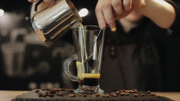 Uma visão próxima de um barman derramando suco de laranja em um copo de vidro latte com líquido preto nele — Vídeo de Stock