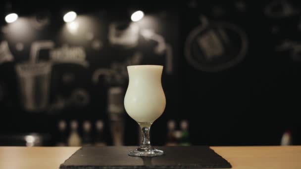 Μια κοντινή όψη ενός γυαλιού γεμάτο μιλκσέικ σε ένα πάγκο μπαρ. Αρσενικό μπάρμαν που βάζει δύο καλαμάκια στο ποτό — Αρχείο Βίντεο