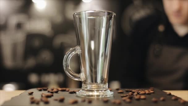 Un primo piano di una tazza di vetro vuoto per il latte in piedi su un bancone di un bar con alcuni chicchi di caffè su di esso — Video Stock