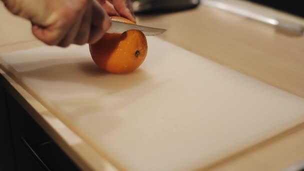 Un primer plano de manos masculinas cortando una naranja fresca en una tabla de cortar blanca — Vídeos de Stock