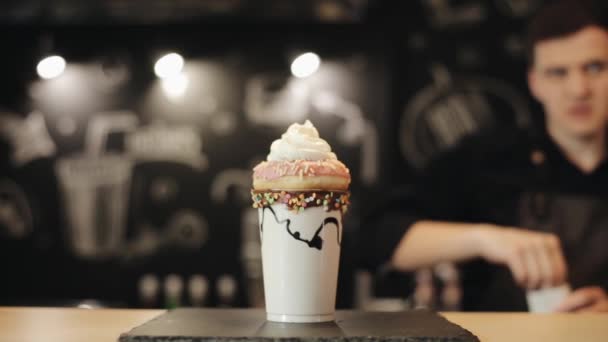 Ένα αρσενικό με χέρι που σπάλισμα ζαχαροπλαστικής ντύσιμο πάνω από μιλκσέικ με ντόνατ και σαντιγί κρέμα — Αρχείο Βίντεο