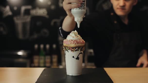 Pouring liquid chocolate and putting a chocolate wafer bar on extreme milkshake with a pink doughnut and whipped cream — Stock Video