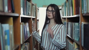 Bobruisk, Beyaz Rusya - 15 Haziran 2019: Uzun siyah saçlı güzel genç kız kütüphanedeki raflar arasında.