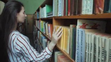 Ellerin kapatın Akıllı görünümlü ve beyaz gömlek ve kolaj okul kütüphanesinde gözlük güzel genç kız okumak için kitap seçerek
