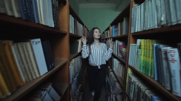 Bobruisk, Bělorusko-15. června 2019: hezká mladá dívka s dlouhými černými vlasy prochází mezi policemi v knihovně. Zpomaleně — Stock video