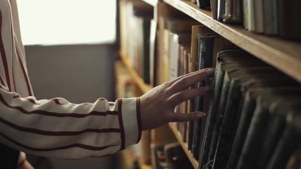 Primer plano de las manos femeninas en busca de un libro de una estantería en la biblioteca — Vídeos de Stock