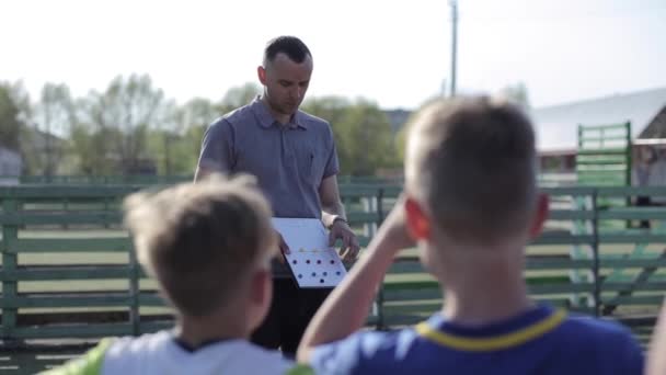 Joven entrenador entrenador de fútbol entrenar a los niños utilizando la estrategia táctica pizarra magnética. Entrenador de fútbol explicando tácticas de partidos al equipo de fútbol infantil . — Vídeos de Stock
