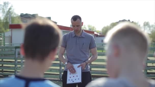 Joven entrenador entrenador de fútbol entrenar a los niños utilizando la estrategia táctica pizarra magnética. Entrenador de fútbol explicando tácticas de partidos al equipo de fútbol infantil . — Vídeos de Stock