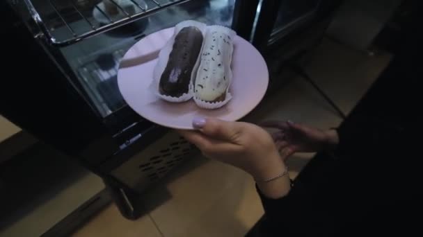 Un primer plano de una mano femenina poniendo un plato con eclairs en la nevera y cerrando la puerta de cristal — Vídeos de Stock