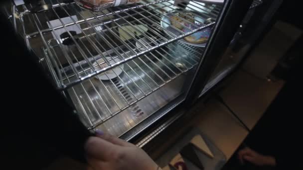 Женская рука берет тарелку с чизкейками в холодильнике — стоковое видео