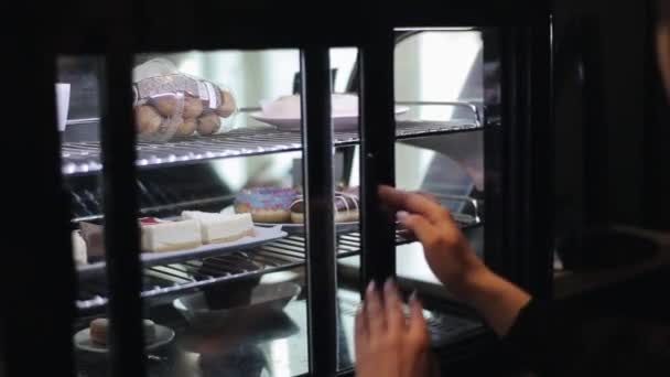 Um close-up de uma mão feminina colocando uma placa com eclairs fora da geladeira e fechando a porta de vidro — Vídeo de Stock