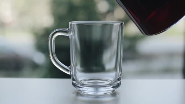 Pemandangan dekat menuangkan teh hitam dari teko gelas ke gelas kosong — Stok Video