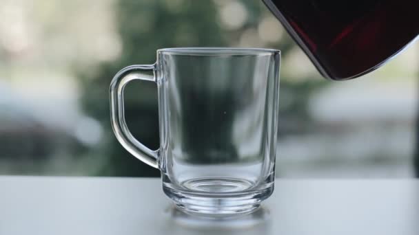 Une vue rapprochée de verser du thé noir d'une théière en verre dans une tasse en verre vide 