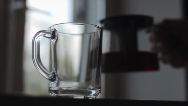 Uma visão próxima de derramar chá preto de um bule de vidro em uma xícara de vidro vazia — Vídeo de Stock