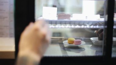 Bir dükkan penceresinin arkasında üç makaron ile bir tabak yakın çekim