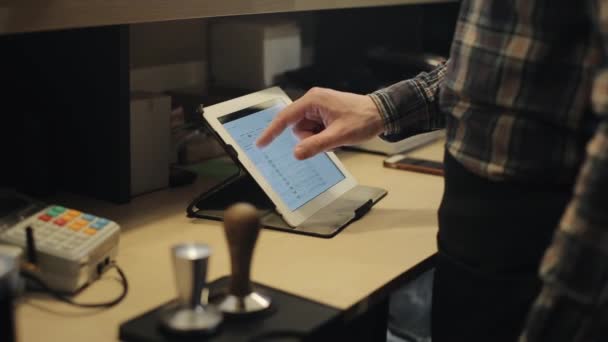 Een close-up van een mannelijke kassier met een touchpad achter een teller in een koffieshop — Stockvideo