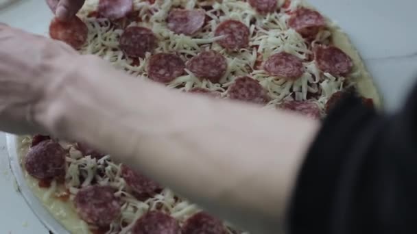 Un primer plano de una mano masculina poniendo salami en pizza cruda — Vídeos de Stock