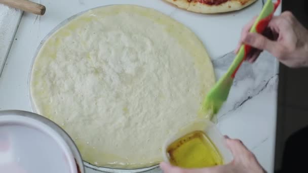 Sebuah close-up dari tangan manusia menerapkan minyak zaitun pada adonan pizza menggunakan silikon kuas — Stok Video