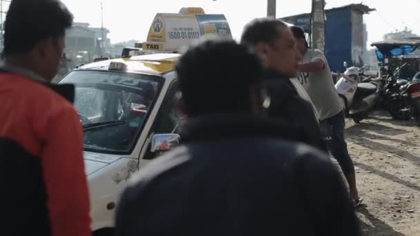 Kathmandu, Nepal - 27 de novembro de 2019: Um motorista de táxi nepali lava seu carro ao lado de uma estrada da cidade limpando-o com um pano e conversando com homens que passam apontando seu dedo para longe. Close-up — Vídeo de Stock