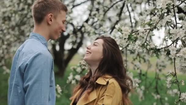 Ένα ρομαντικό ραντεβού σε έναν ανθισμένο κήπο. Ένας νεαρός φιλάει τον εραστή του και της πετάει πέταλα λουλουδιών. Κοντινό πλάνο. Αργή κίνηση — Αρχείο Βίντεο