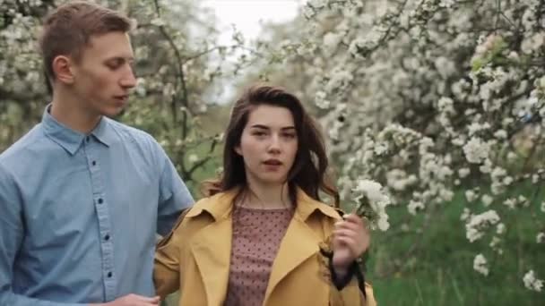 Un chico joven y atractivo abraza a su hermosa novia caminando por el floreciente jardín de primavera. Primer plano. En cámara lenta. — Vídeo de stock