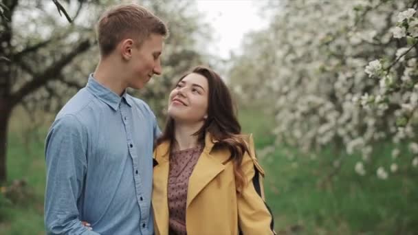 Ett ungt lyckligt par går på vårdagen i en blommande trädgård. Milda romantiska känslor. En kärlekshistoria. Närbild. Långsamma rörelser — Stockvideo