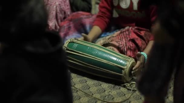 Nepálská mladá indická dívka v jasných šatech hraje na národní buben šílence, který sedí na podlaze místnosti. Detailní záběr. Rozmazané přední pozadí — Stock video