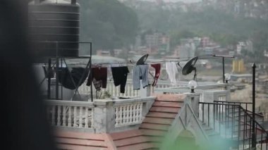 Asya 'da bir apartmanın çatısının manzarası. Çatıda su tankları ve uydu anteni var. Güzel çitler ve kurutucu elbiseler.