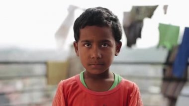 Katmandu, Nepal - 27 Kasım 2019: Utangaç Hintli bir Nepalli çocuğun portresi bir evin çatısında ipte çırpınan kıyafetlerin olduğu bir zemin üzerinde duruyor. Yüzünde tuhaf bir ifade var. İstekler