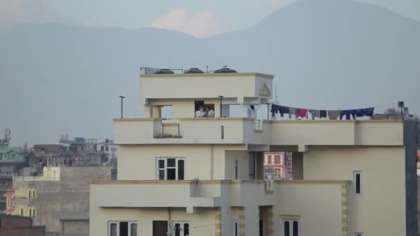 Katmandu, Nepal. Widok na dach jednego z budynków mieszkalnych na tle gór. Na dachu są dwie białe młode dziewczyny rozmawiające przez telefon i śmiejące się — Wideo stockowe