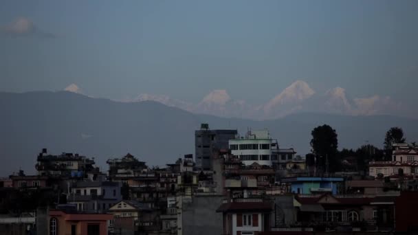 Bella vista di case urbane sullo sfondo di cime innevate di alte montagne. Silhouette di una catena montuosa contro il cielo blu e uccelli volanti — Video Stock