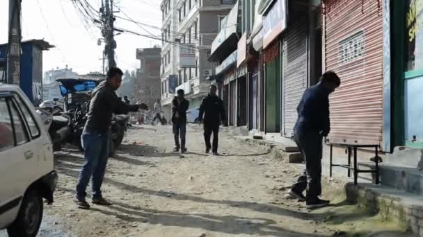 Kathmandu, Nepal - 27 novembre 2019: Un giovane indiano nepalese legge un giornale seduto su una panchina in strada di fronte a un tassista che lava la sua auto. La vita urbana quotidiana. Primo piano — Video Stock