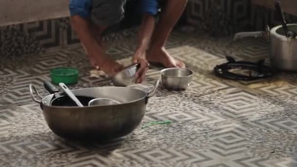 El joven indio nepalí lava cuidadosamente cuencos de hierro con un trapo en cuclillas en el suelo con hermosas baldosas. Primer plano — Vídeo de stock