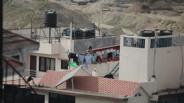 カトマンズ、ネパール- 27 11月2019:建設現場の背景にある住宅の屋根の上のロープの上に、空のインドのネパールの少女がぬれた服をぶら下げている — ストック動画