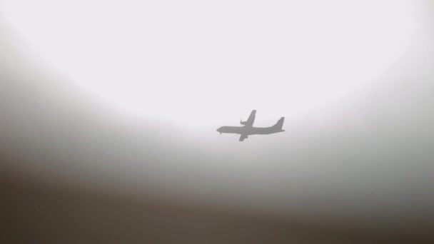 La silhouette dell'aereo che vola attraverso il cielo grigio. L'aereo si nasconde dietro un primo piano nero sfocato e riappare. Concetto di viaggio. Rallentatore — Video Stock