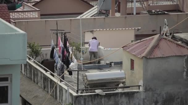 Катманду, Непал - 27 листопада 2019: Катманду, Непал. Щоденне життя міста. Чоловік у тюрбані стирає одяг на даху. Одяг сушать на канатах. Виснаження. Погляд ззаду — стокове відео