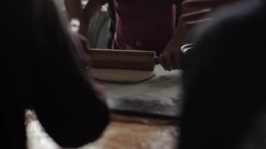 Ev yapımı pizza konusunda yüksek lisans. Çocuklar pizza yapar. Çocuk hamuru yuvarlıyor ve yetişkinler ona yardım ediyor. Arka planda bulanıklık. Yakın plan.