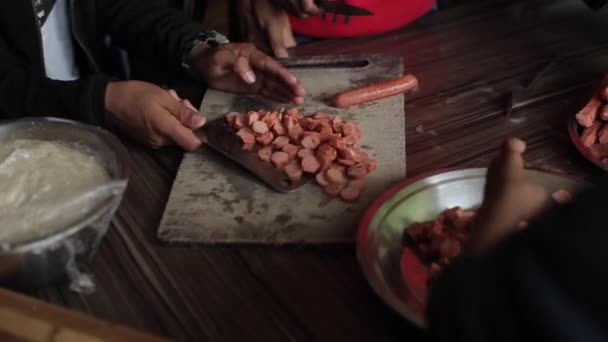 Niños indios nepalíes preparan pizza en la cocina de un orfanato. Los adolescentes cortan un montón de salchichas juntas y las ponen en un tazón de metal grande. Vista desde un lado. Primer plano — Vídeos de Stock