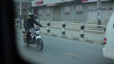 Delhi, Hindistan - 29 Kasım 2019: Katmandu. Nepal 'de. Kasklı bir motosikletçi ve sırtında sırt çantası olan siyah bir ceket şehrin işlek yollarında geziniyor. Arabanın camından ateş ediliyor.