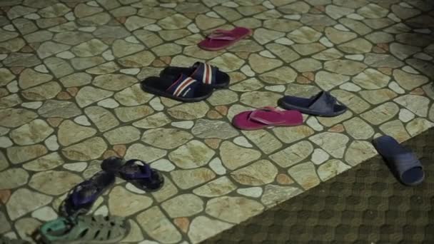 Дети разноцветные резиновые туфли шлепанцы разных размеров стоят на полу в коридоре на красивой каменной плитке. Крупный план — стоковое видео
