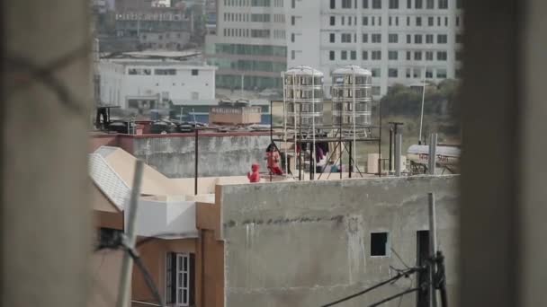 Kathmandu, Nepal - 27 novembre 2019: Una vivace bambina indiana nepalese appende vestiti bagnati su una corda sul tetto di una casa di abitazione sullo sfondo di un cantiere — Video Stock