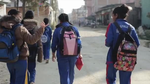 Delhi, India - 29 November 2019: Gadis sekolah India Nepal berjalan di sepanjang jalan kota yang sempit melewati mobil dan bangunan perumahan. Pandangan ke belakang. Gerakan lambat — Stok Video