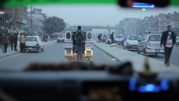 Kathmandu, Nepal - 14 de novembro de 2019: Um jovem nepalês indiano monta um microônibus em pé em plena altura em um vagão em uma estrada movimentada na cidade noturna. Visão traseira — Vídeo de Stock