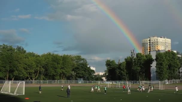 Mińsk, Białoruś - 23 czerwca 2020: Drużyna piłkarska trenuje i gra w piłkę nożną na otwartym stadionie na tle jasnej tęczy na zachmurzonym niebie — Wideo stockowe