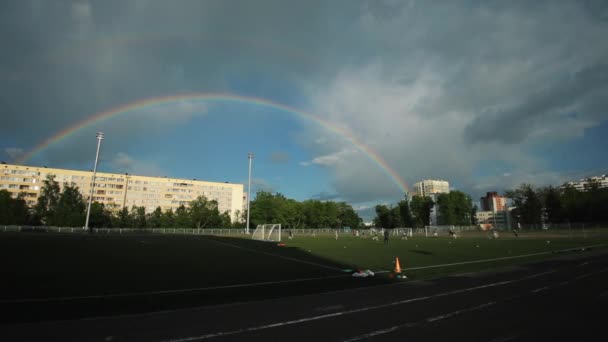 Minsk, Bielorrússia - 23 de junho de 2020: Vista do arco-íris sobre a cidade e sobre o campo de futebol onde a equipe de futebol está treinando — Vídeo de Stock